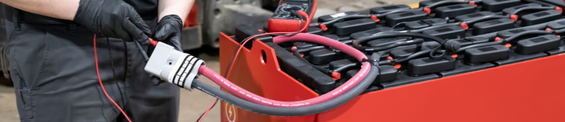 Technician using a meter to inspect an industrial forklift battery.
