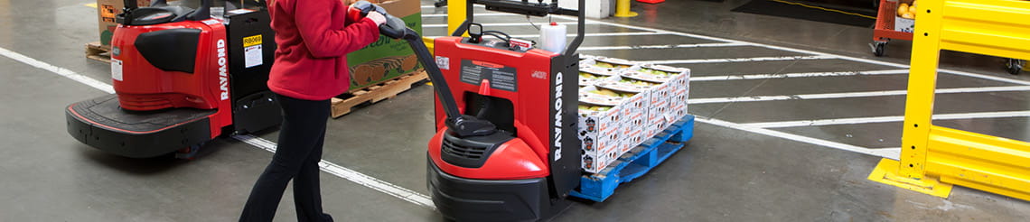 Warehouse worker operating a Raymond 8210 electric pallet truck in a distribution center.