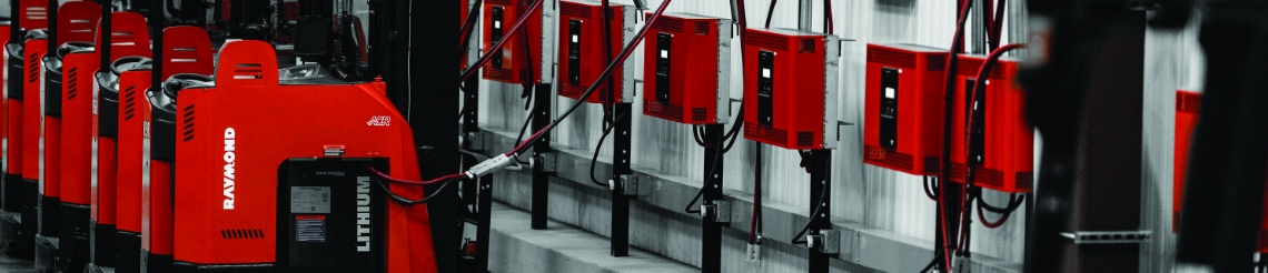 Raymond electric forklifts connected to warehouse wall-mounted charging stations.