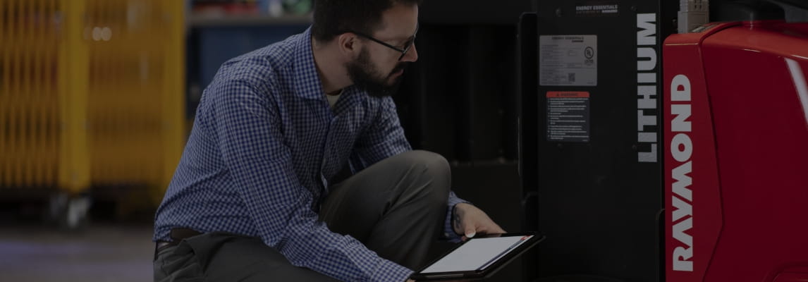 RSC employee holding a tablet inspecting a Raymond forklift and lithium-ion battery in warehouse.
