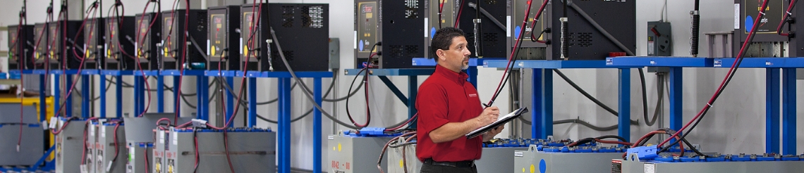 RSC energy specialist with a clipboard reviewing a line of power systems on a warehouse wall.