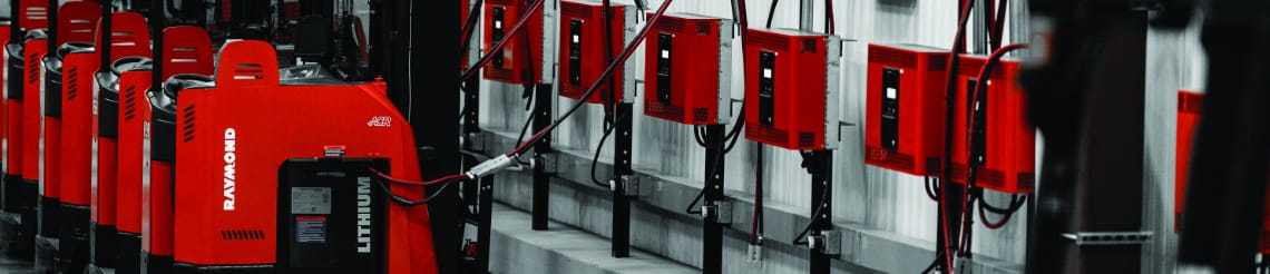 Red Raymond forklifts lined up to warehouse wall charging stations.