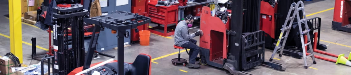 RSC shop technician wearing a respirator sanding a used forklift in the RSC Cincinnati shop. He's surrounded by a workbench and other used forklifts. 