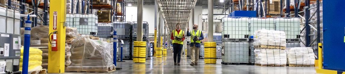 RSC specialist walks through facility with customer in safety vest. The walk in the middle of racking aisles with pallets at the end of each aisle.