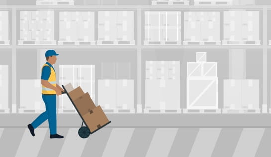 Person walking with load of boxes on hand cart in gray warehouse.