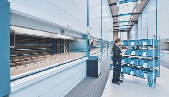 Worker looking at a cart of totes next to a vertical lift module in warehouse.