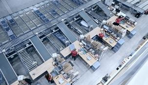 Multiple conveyors leading to warehouse packing stations where workers pack orders.