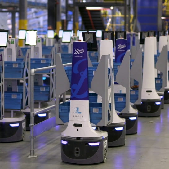 White and blue Locus autonomous robots driving orders to workers in warehouse.