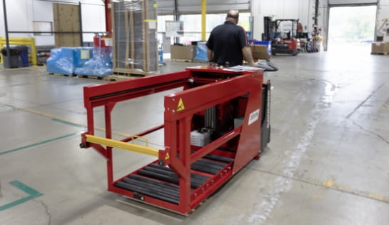Male warehouse worker pulling a pallet jack with a battery extractor attached in dock area.