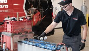 RSC technician spraying at lead acid battery in a warehouse next to an RSC service van.