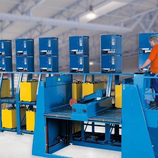 Man working a semi-automated forklift battery handling system in a warehouse. Extractor placing spent batteries onto shelves to re-charger on battery chargers.