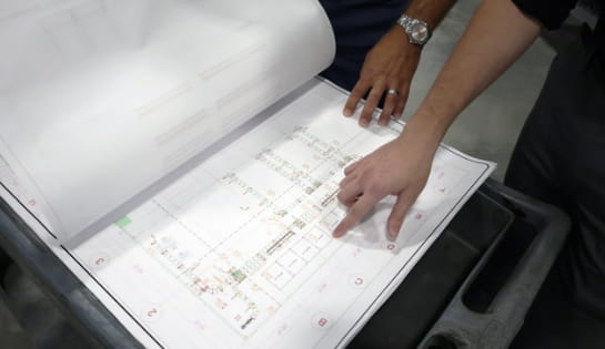 Warehouse blueprint laid out on table with two hands pointing at sections of the drawing.