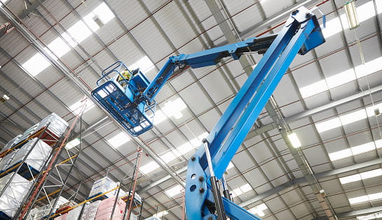 Looking up at an extended blue boom lift in a warehouse