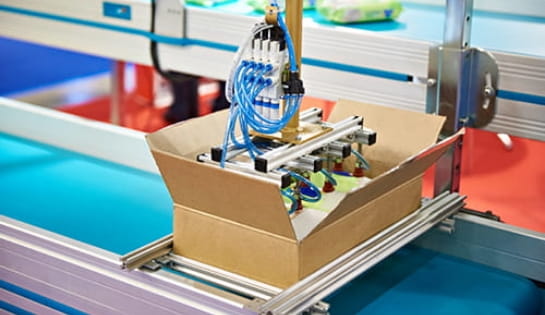 Case packing robot arm placing product into box on assembly line.