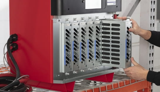 Two hands pulling a module out of an industrial battery charger sitting on a racking.