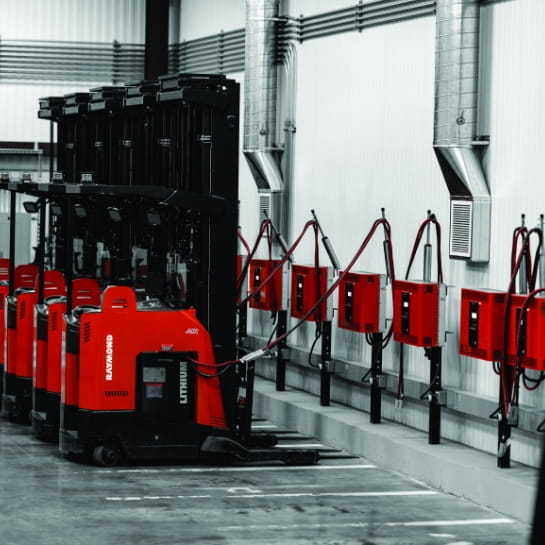Red Raymond forklifts lined up to warehouse wall charging stations. 