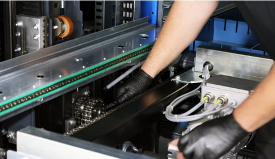 Technician's gloved hand checking the chains and gears inside of an AS/RS.