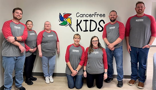 RSC volunteering employees pose in front of CancerFree KIDS sign.