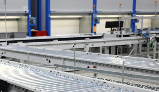 Conveyor running across and back in front of picking stations and vertical lift modules.