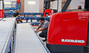 Technicians working on a set of automated conveyors next to a Raymond forklift.