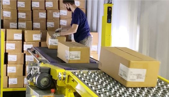 Worker unloading a trailer full of boxes onto a Destuff-it conveyor belt.
