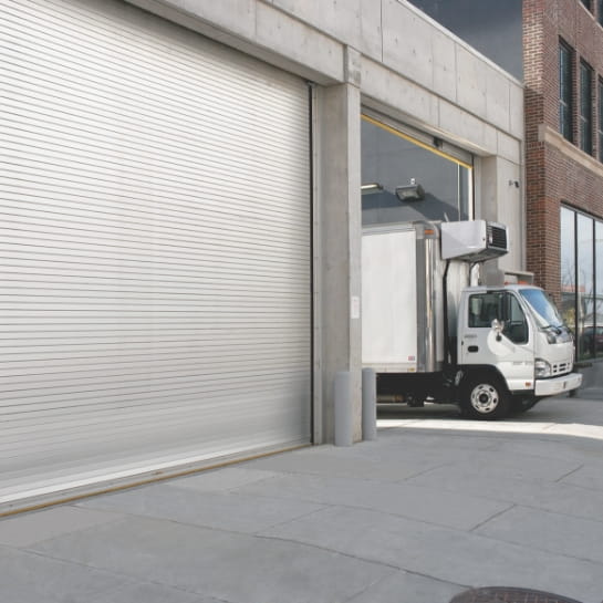 Box truck leaving a warehouse dock area through a dock door.
