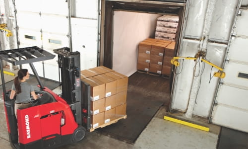 Forklift driving pallet of boxes into truck in interior warehouse dock