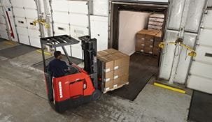 Forklift driving pallet of boxes into truck in interior warehouse dock.