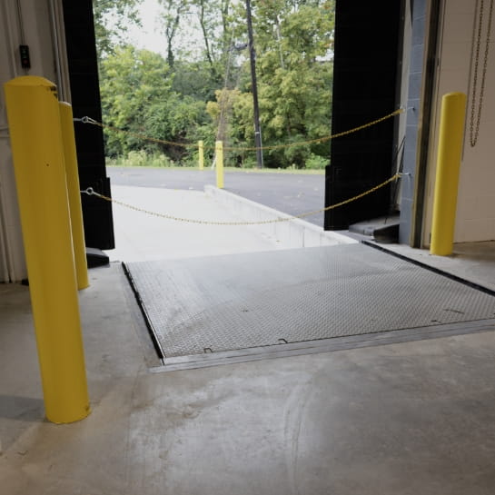 A receiving area of a warehouse with a view of an open dock door and leveler.