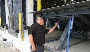 Raymond Storage Concept technician lubricating dock leveler at warehouse dock.