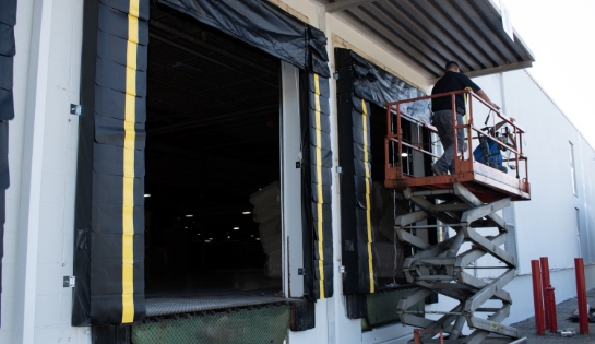 Two men on a scissor lift installing a dock door on a warehouse