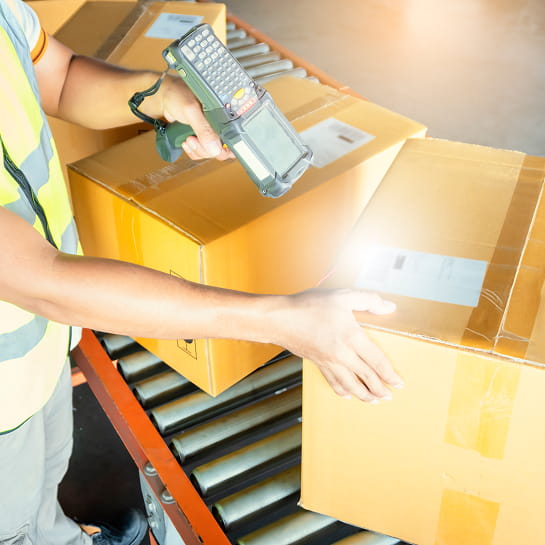 Warehouse worker in safety vest scanning a package on conveyor belt.