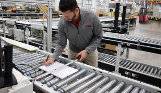 RSC engineer measuring a conveyor section and taking notes in a warehouse.
