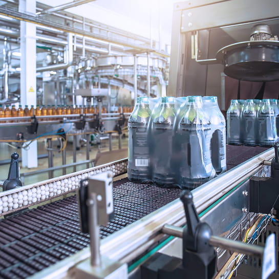 Beverage bottles leave shrink wrapper on conveyor belt in a bottling plant.