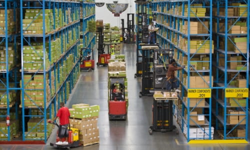 Busy warehouse aisle with several forklifts either driving through or picking orders from racking.
