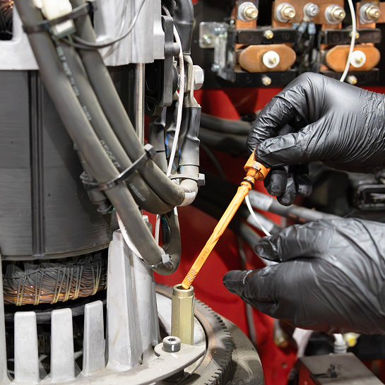 Gloved technician hand checking oil stick in a Raymond forklift engine.