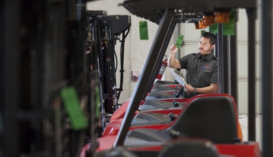 RSC employee in black shirt checking a green tag hanging from a forklift. Several forklifts lined up in a row.