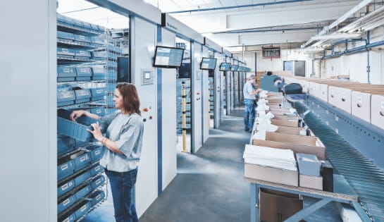 Female worker pulling product from a bin that's housed in a horizontal carousel. 