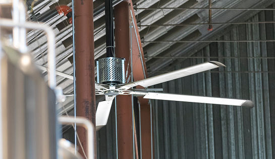 Industrial fan between ceiling rafters in a warehouse.