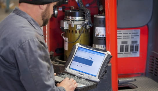 Technician reviewing iWAREHOUSE asset maintenance manager for repair history in front of a forklift engine.