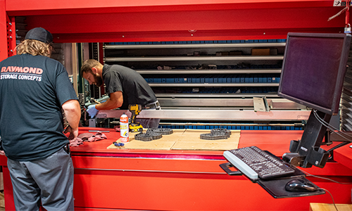 Two technicians in black Raymond Storage Concepts shirts installing a red Kardex Remstar AS/RS.