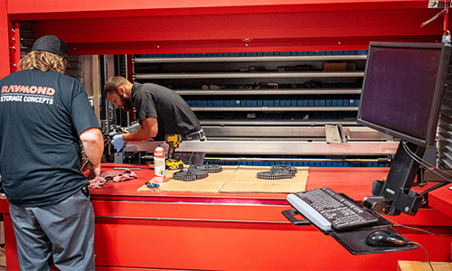 Two technicians in black Raymond Storage Concepts shirts installing a red Kardex Remstar AS/RS.