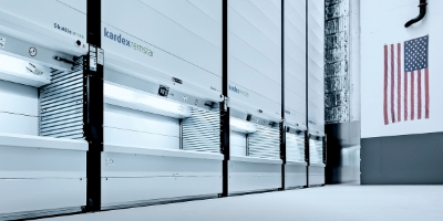 Row of Kardex shuttle vertical lifts in a warehouse. American flag hangs on the wall.