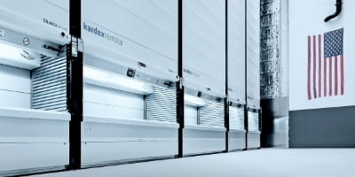 Row of Kardex shuttle vertical lifts in a warehouse. American flag hangs on the wall.