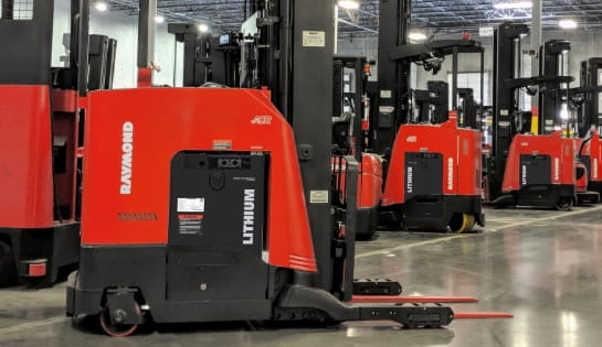 Several standing Raymond counterbalanced forklifts using lithium-ion batteries in a warehouse.