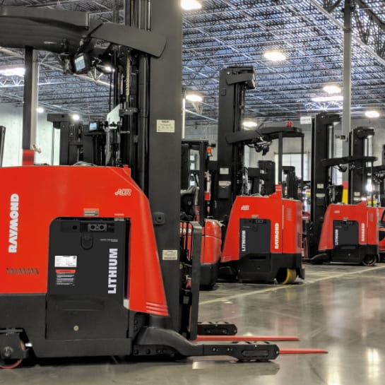 Several standing Raymond counterbalanced forklifts using lithium-ion batteries in a warehouse.