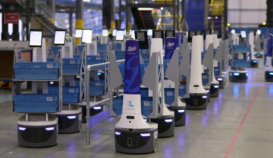White and blue Locus autonomous robots driving orders to workers in warehouse.