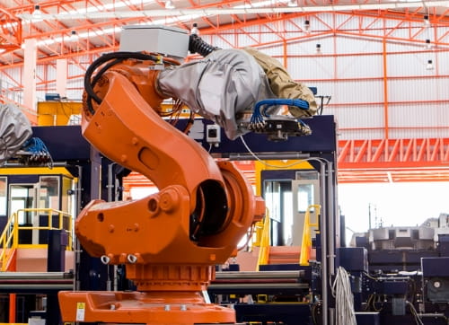 Orange robotic arm in outdoor construction area.