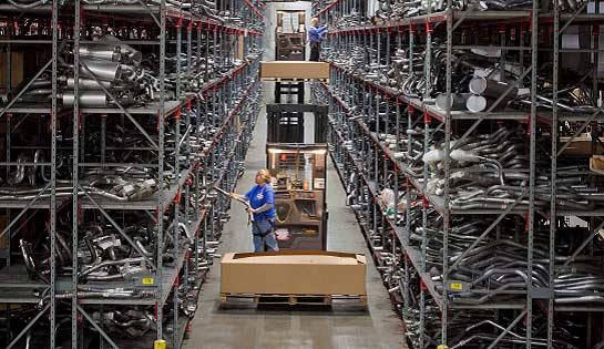 Orderpicker and driver in warehouse aisle picking automotive parts from racking.