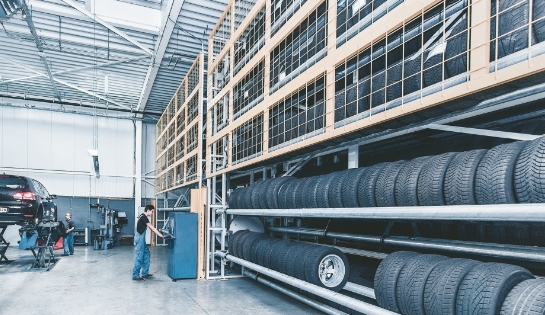 Male worker operating the controls for an oversize product AS/RS that houses vehichle tires inside a auto shop.